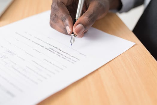 手持钢笔在桌面签署文件 Hand holding pen signing document on desk.